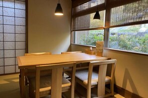 Une table à manger en bois, avec des chaises, un luminaire suspendu et une fenêtre donnant sur un paysage verdoyant.