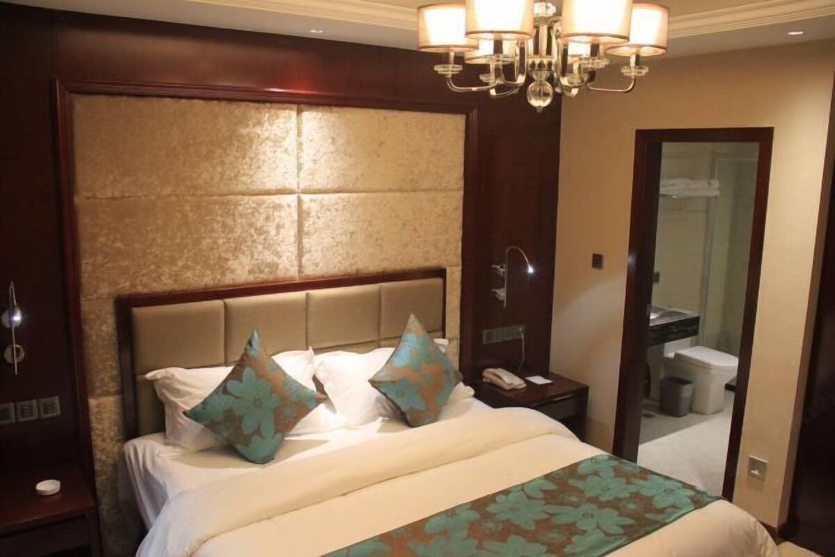 A hotel room with a large bed, a nightstand, a mirror, and a chandelier.