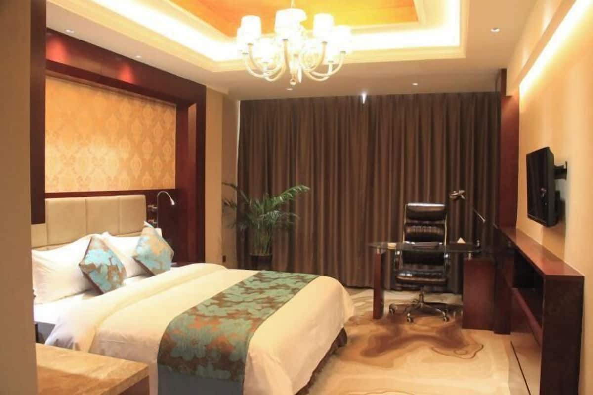 A hotel room with a large bed, a desk, a chair, a television, and a chandelier.