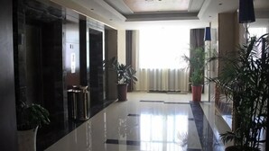Un vestíbulo de hotel con piso pulido, plantas en macetas y un amplio ventanal con cortinas.