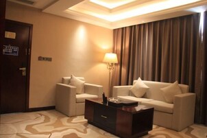 Una habitación de hotel con un conjunto de sofás, una mesita de centro, una lámpara y una alfombra estampada.