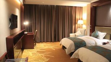 A hotel room with two beds, a desk, a chair, a TV, and a large window with curtains.