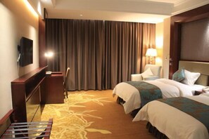 Une chambre d’hôtel avec deux lits, un bureau, une chaise, une télévision et une grande fenêtre avec des rideaux.