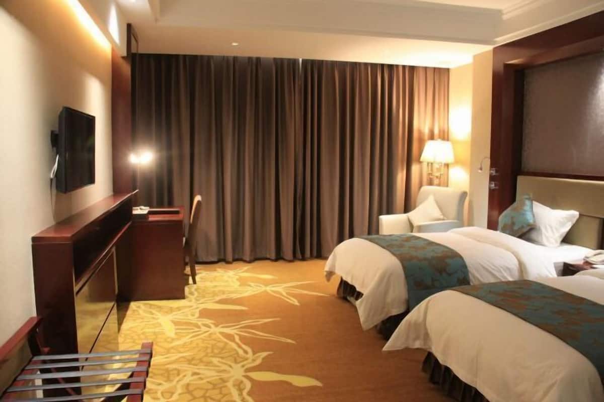 A hotel room with two beds, a desk, a chair, a TV, and a large window with curtains.