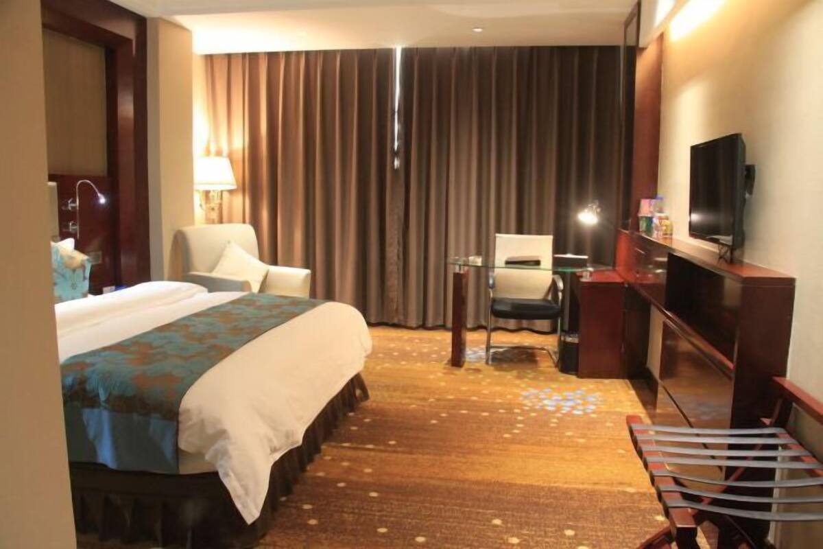 A hotel room with a bed, a desk, a chair, a television, and a large window with curtains.