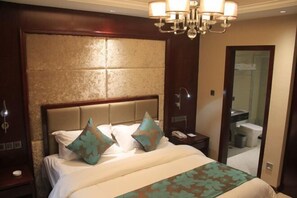 Une chambre d’hôtel avec un grand lit, un lustre, une table de chevet et un miroir.