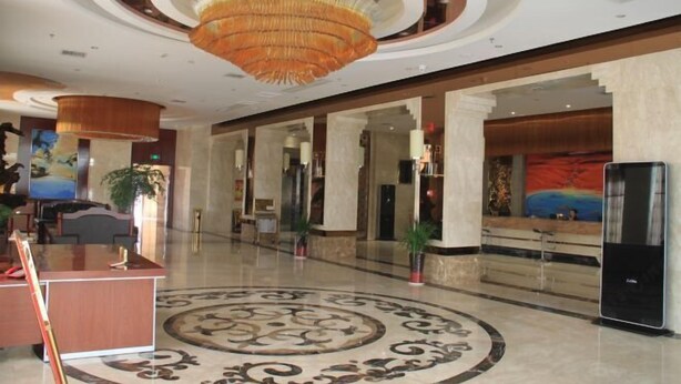 Un hall amplio con una alfombra circular de diseño, un mostrador de recepción y una lámpara de araña moderna.