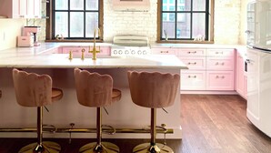 A kitchen with pink cabinets, a central island with stools, a white stove, and large windows with patterned curtains. - NEW luxury retro loft in heart of historic, walkable Southside district  (Chattanooga)