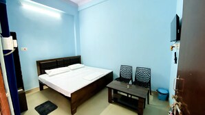 A room with a bed, a small table, two chairs, a TV, and a blue wall. - Hanumat Home Stay (Faizabad)