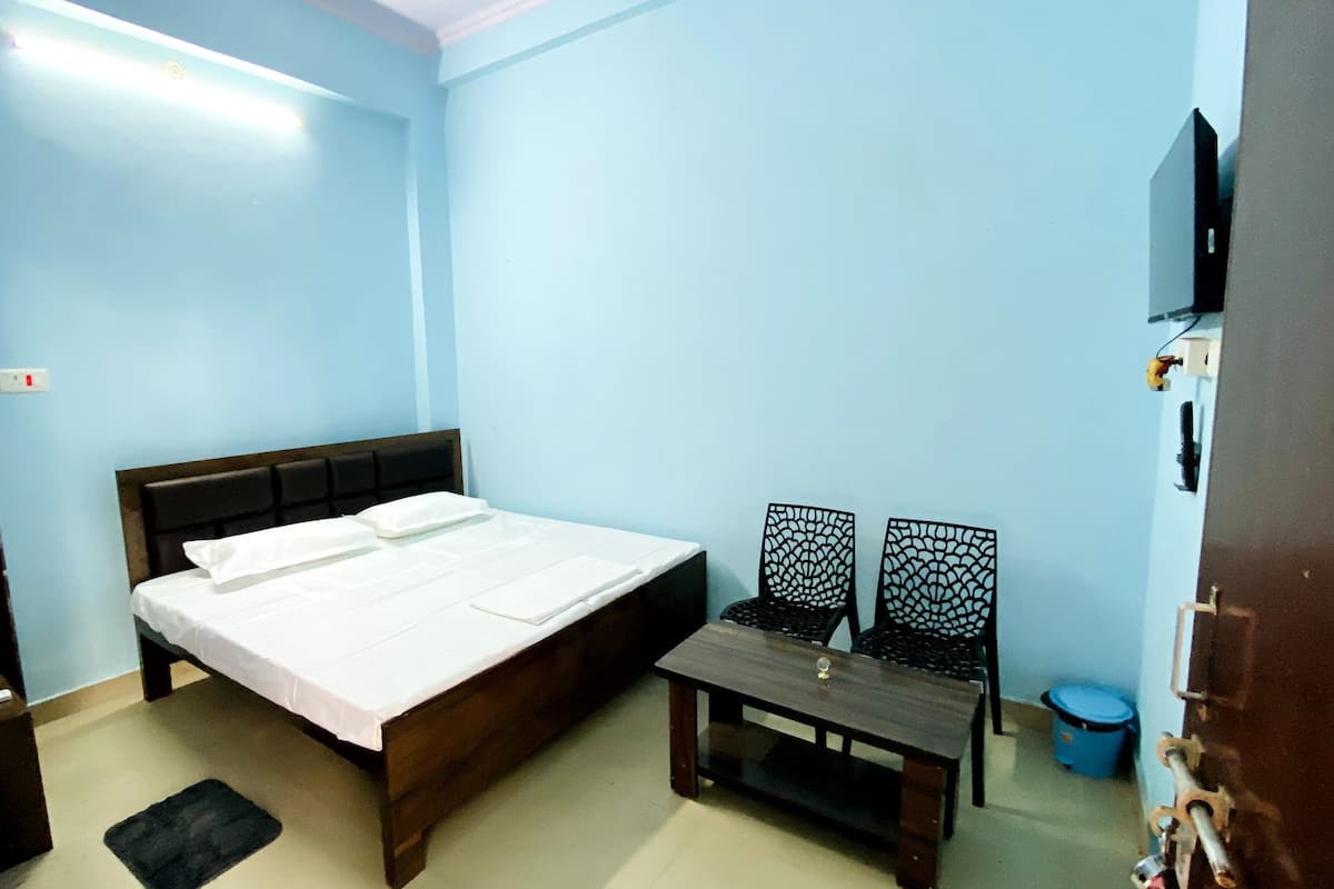 A room with a bed, a small table, two chairs, a TV, and a blue wall.