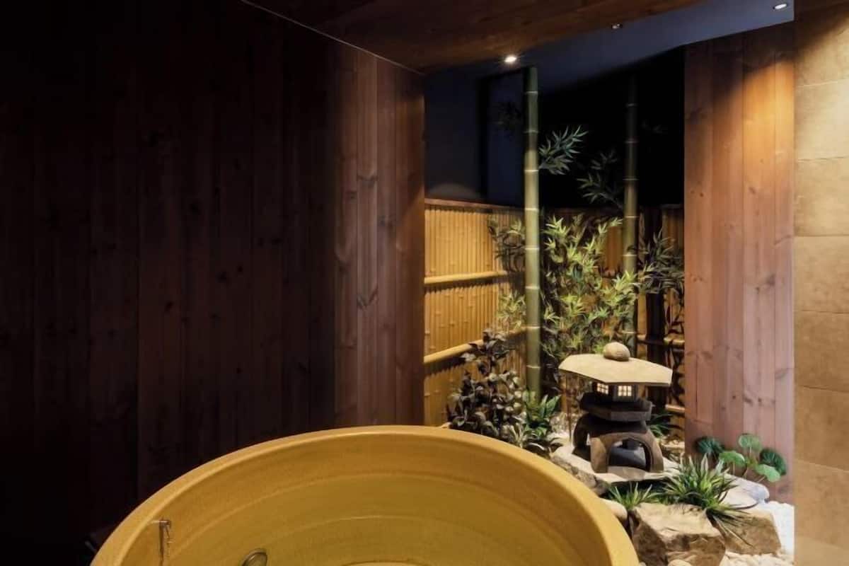A traditional Japanese-style room with a large wooden bathtub, bamboo plants, and a stone lantern.