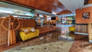 A lobby with a wooden wall, a yellow sofa, a large wooden wheel, and a pool area in the background. - Hotel Plaza Mirador Ciudad del Carmen (Ciudad del Carmen)