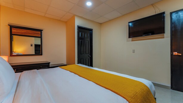 A hotel room with a bed, a bedside table, a mirror, a TV mounted on the wall, and a door. - Hotel Plaza Mirador Ciudad del Carmen (Ciudad del Carmen)