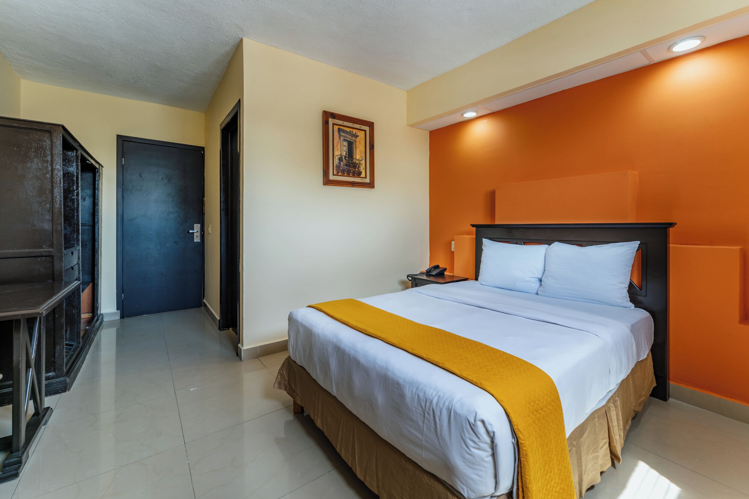 A hotel room with a bed, a nightstand, a desk, and a door.