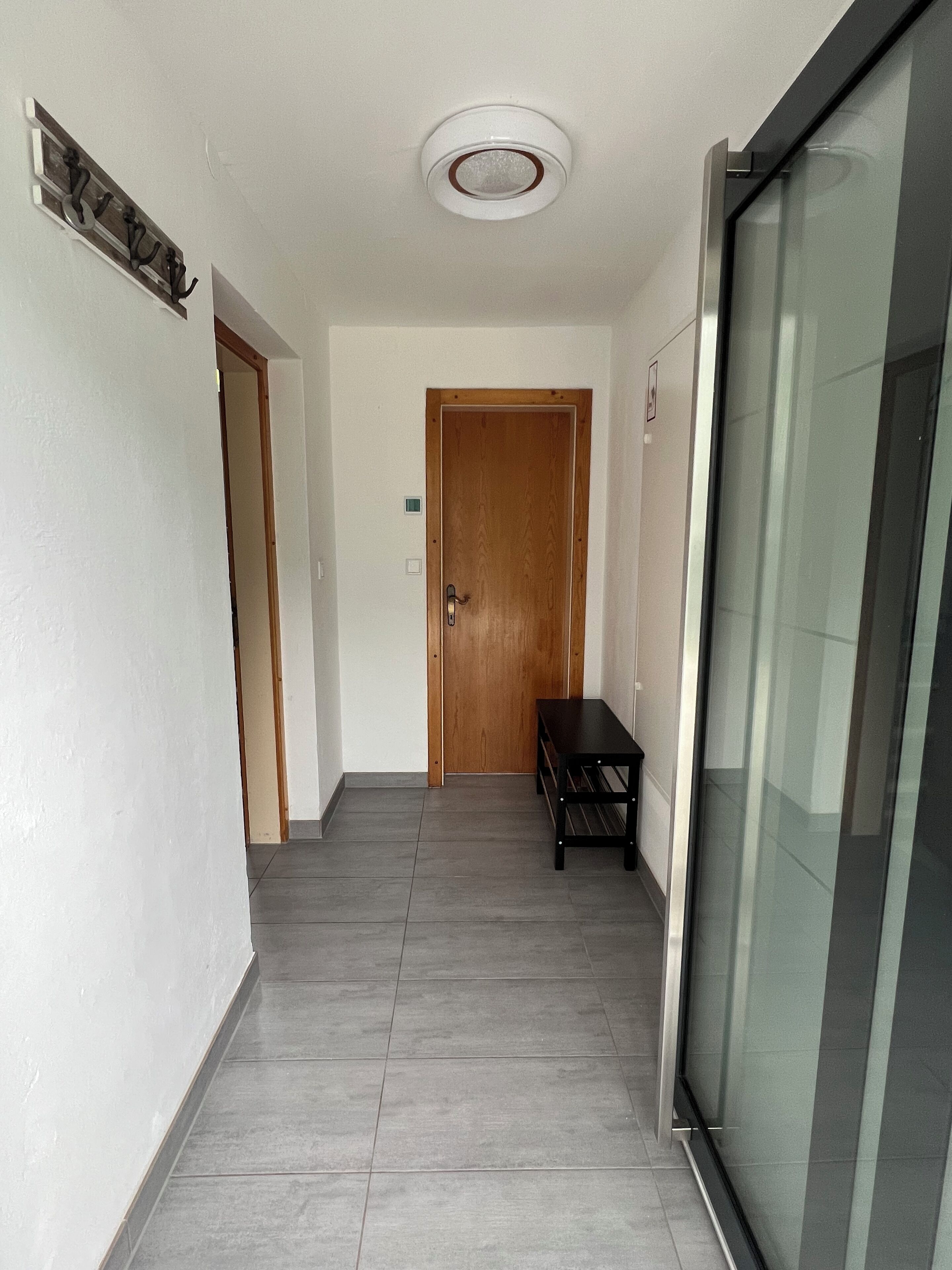 A hallway with a wooden door, a bench, and a glass door on the right.