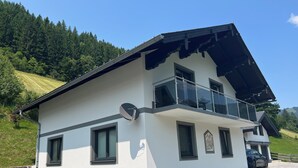 A modern two-story house with a balcony, large windows, and a car parked in the driveway.