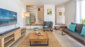 Ein modernes Wohnzimmer mit einem Holztisch, einer Couch mit Kissen, einem Fernseher auf einem Holzbodenständchen, einer Treppe mit Holzwand und einer Wand mit einem gerahmten Bild.