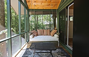 Eine überdachte Veranda mit einer Couch, einem Sessel und einem gemusterten Teppich.