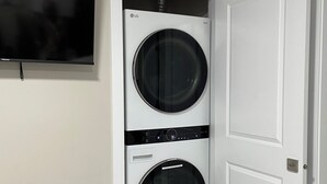 A laundry room with two stacked front-loading washing machines, a wall-mounted television, and a white door.