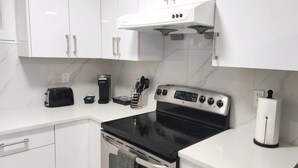 A modern kitchen with white cabinets, a black stove, a coffee maker, and a toaster.