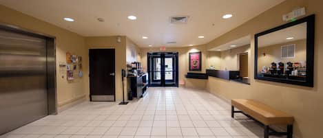 A hotel lobby with a tiled floor, a bench, a reception desk, and a mirror on the wall.