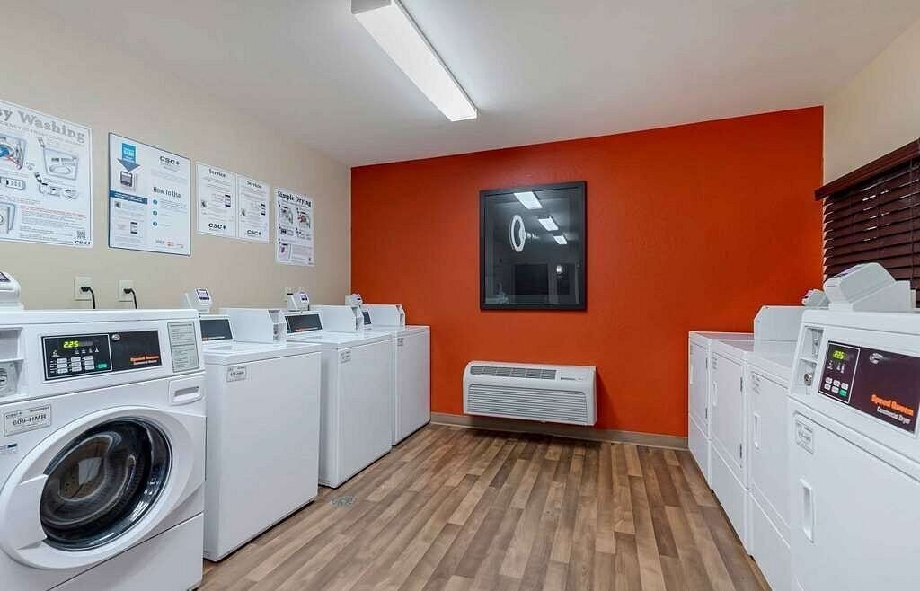 A laundry facility with multiple washing machines, instructional posters on the wall, and a bright orange accent wall.