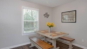 A dining area with a wooden table and benches, a vase with yellow flowers, and a framed picture on the wall. - Grad Basecamp | Pet-Friendly 2BR (Columbus)