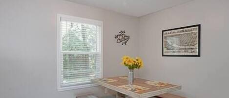 Ein Essbereich mit einem Holztisch, Bänken, einer Vase mit gelben Blumen und einem gerahmten Bild an der Wand.
