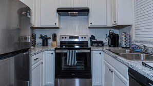 A kitchen with white cabinets, stainless steel appliances, a coffee bar, and a dish rack. - Grad Basecamp | Pet-Friendly 2BR (Columbus)