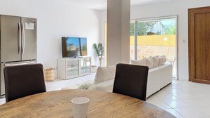 A modern kitchen with a refrigerator, a dining table with a cup, a sofa, and a TV. - Bas de Villa Oasis (Sainte maxime)