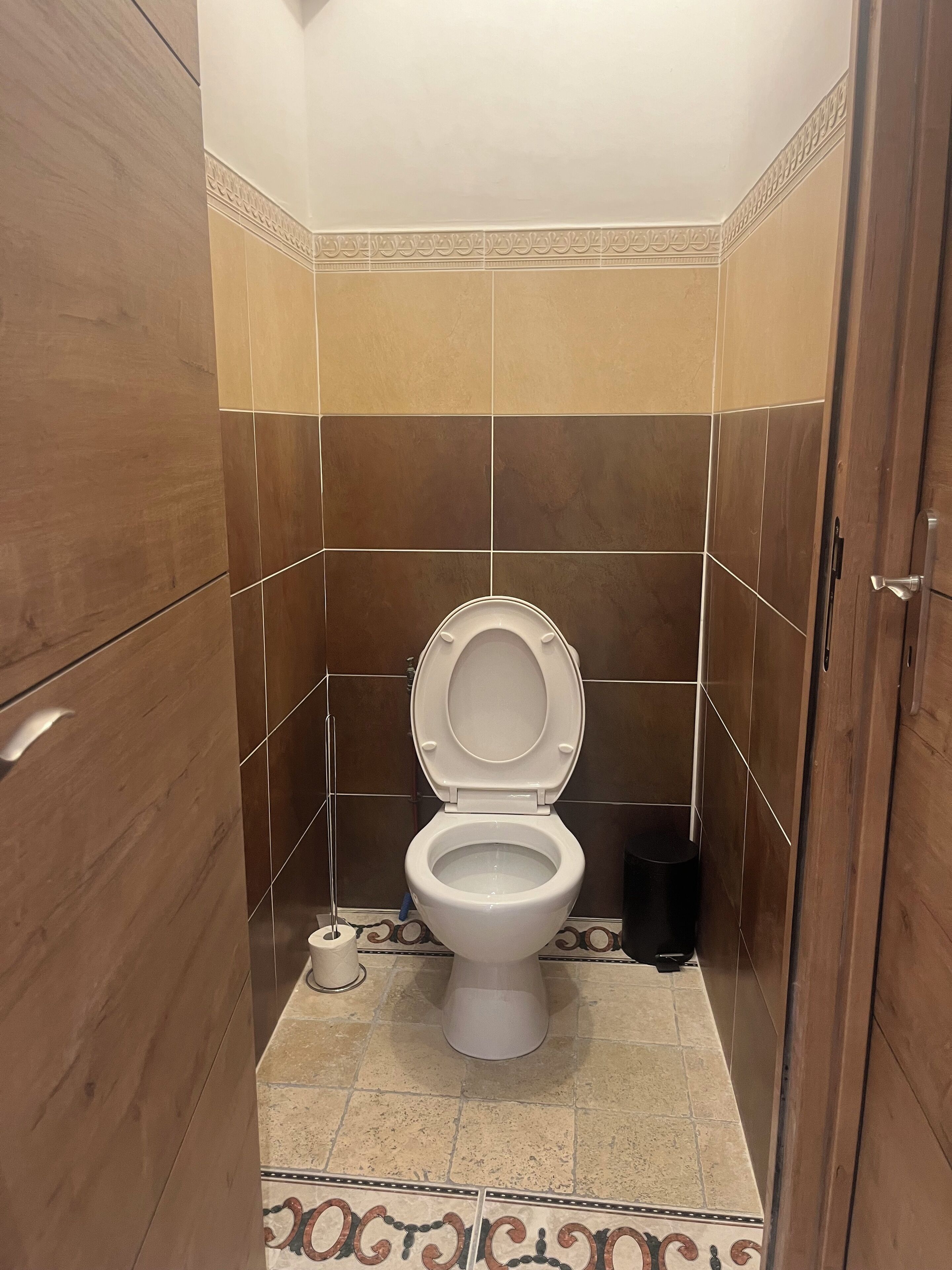 A small, modern bathroom with a toilet, a trash bin, and a patterned floor.