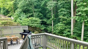 Eine Holzterrasse mit Grill, zwei gestreiften Stühlen und einem Tisch.