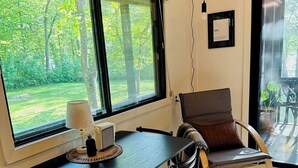 Ein Essbereich mit Tisch und Stühlen, großen Fenstern mit Jalousien, einem gerahmten Zertifikat an der Wand und Blick ins Grüne.