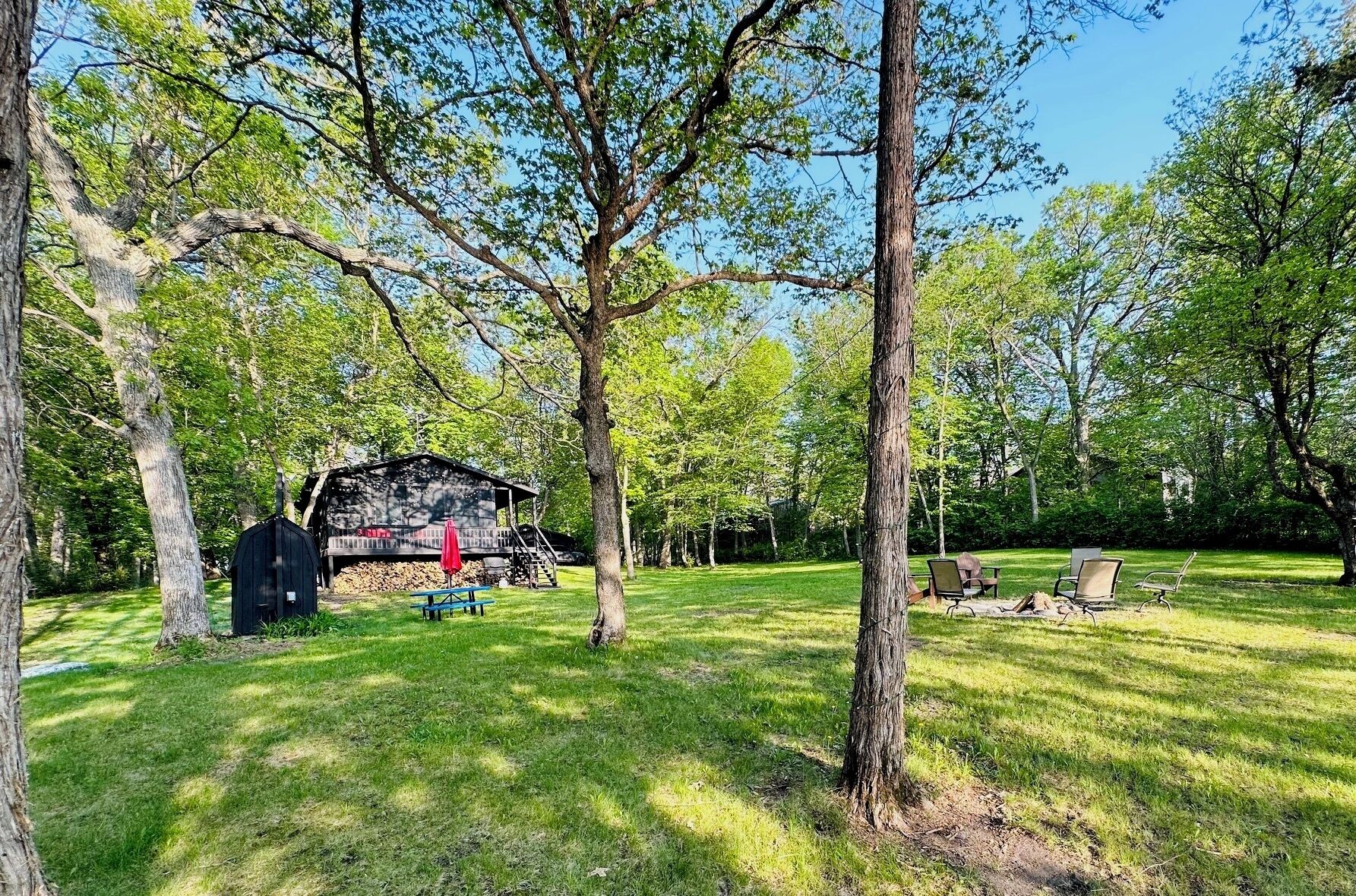 A rustic cabin in a wooded area with picnic tables and outdoor seating.