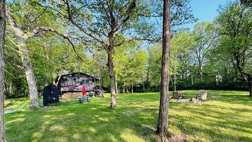 A rustic cabin in a wooded area with picnic tables and outdoor seating.