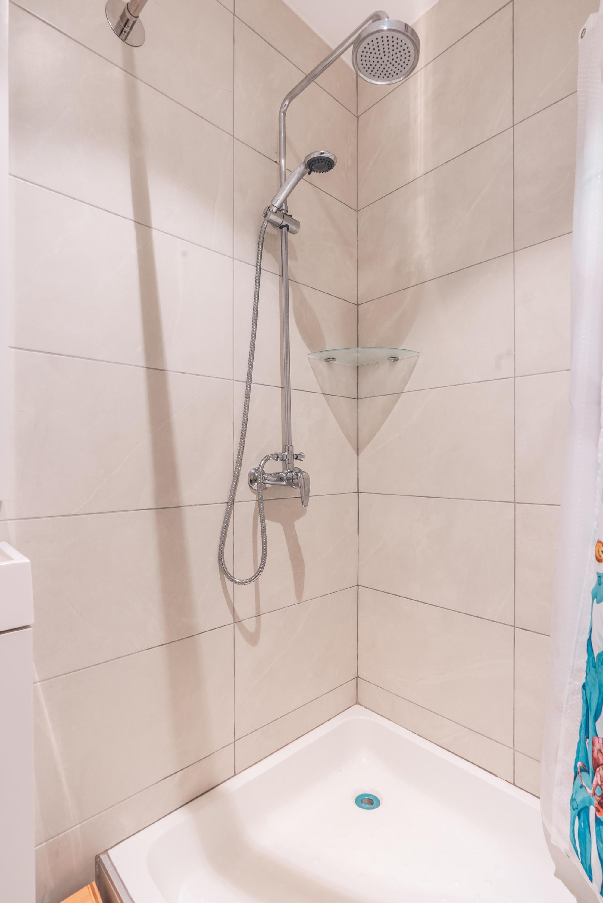 Una ducha con repisa de vidrio, una bañera blanca y pared con azulejos.