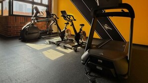 Uma academia com bicicletas ergométricas, esteira e parede com janela.