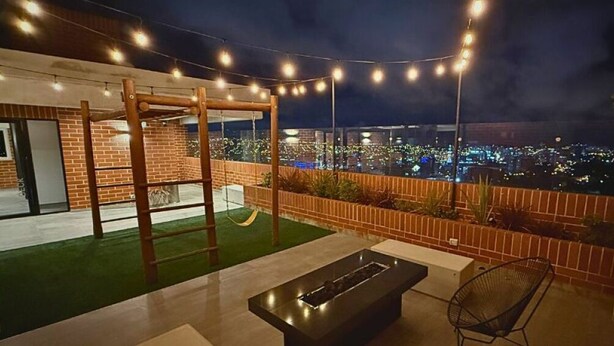 Um pátio externo com lareira, assentos e vista da cidade à noite.