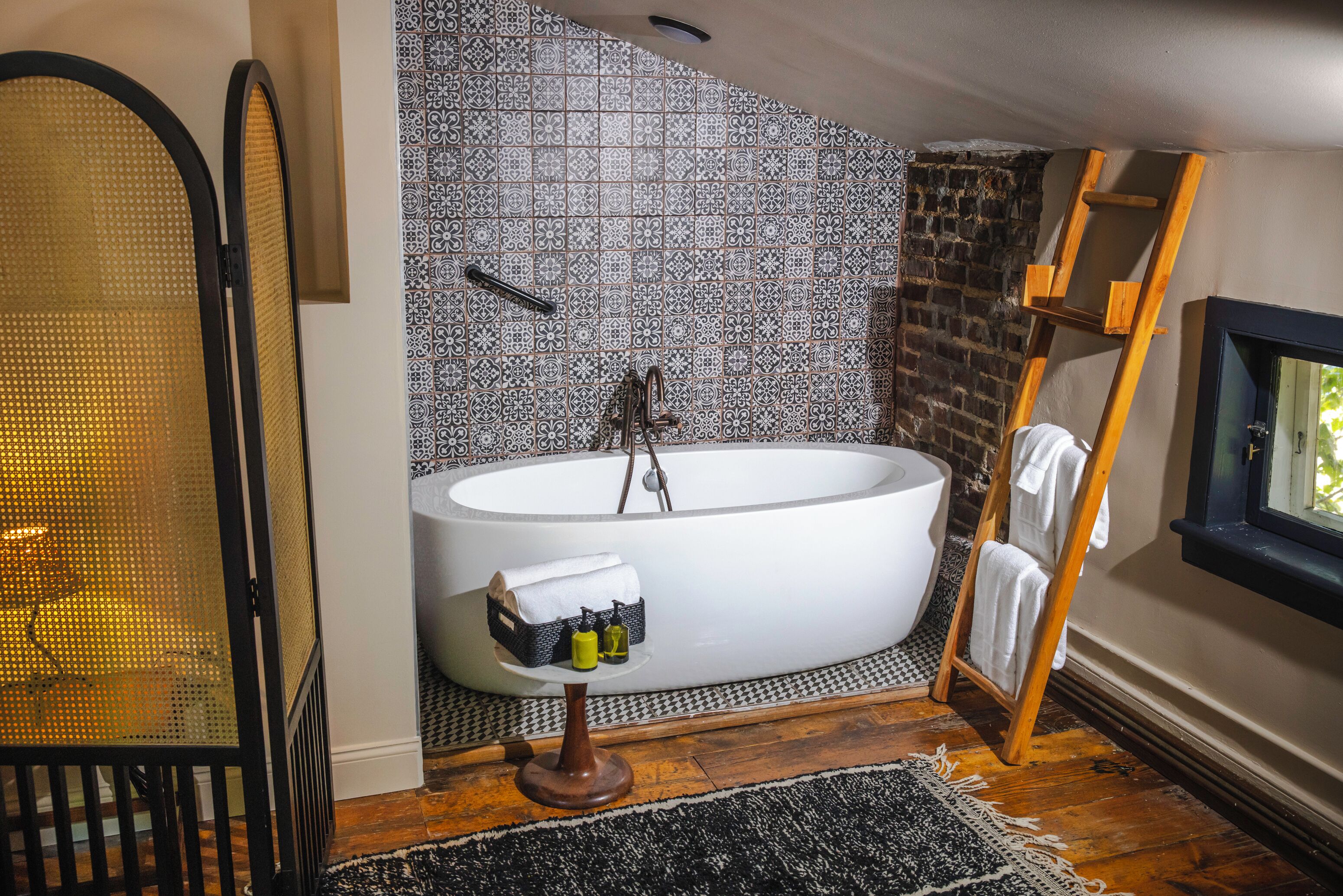 A modern bathroom with a freestanding bathtub, a wooden ladder, and a black and white patterned wall.