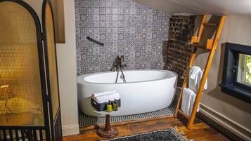 A modern bathroom with a freestanding bathtub, a wooden ladder, and a black and white patterned wall.