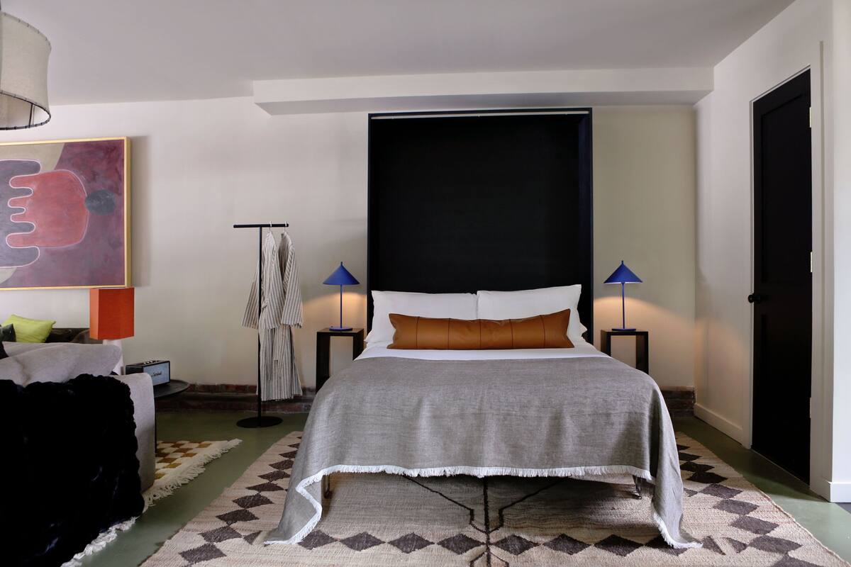 Een moderne slaapkamer met een groot bed, een zwart hoofdeinde en twee bedlampen.