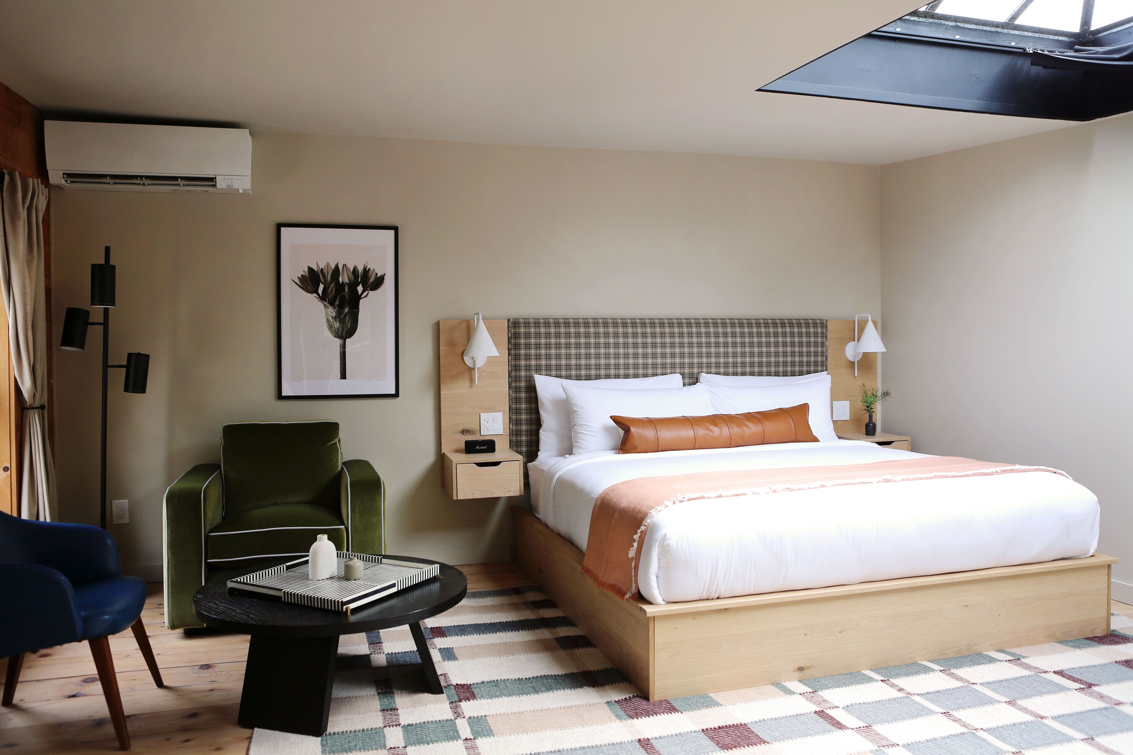 A hotel room with a large bed, a green armchair, a small table with a book, and a framed picture on the wall.