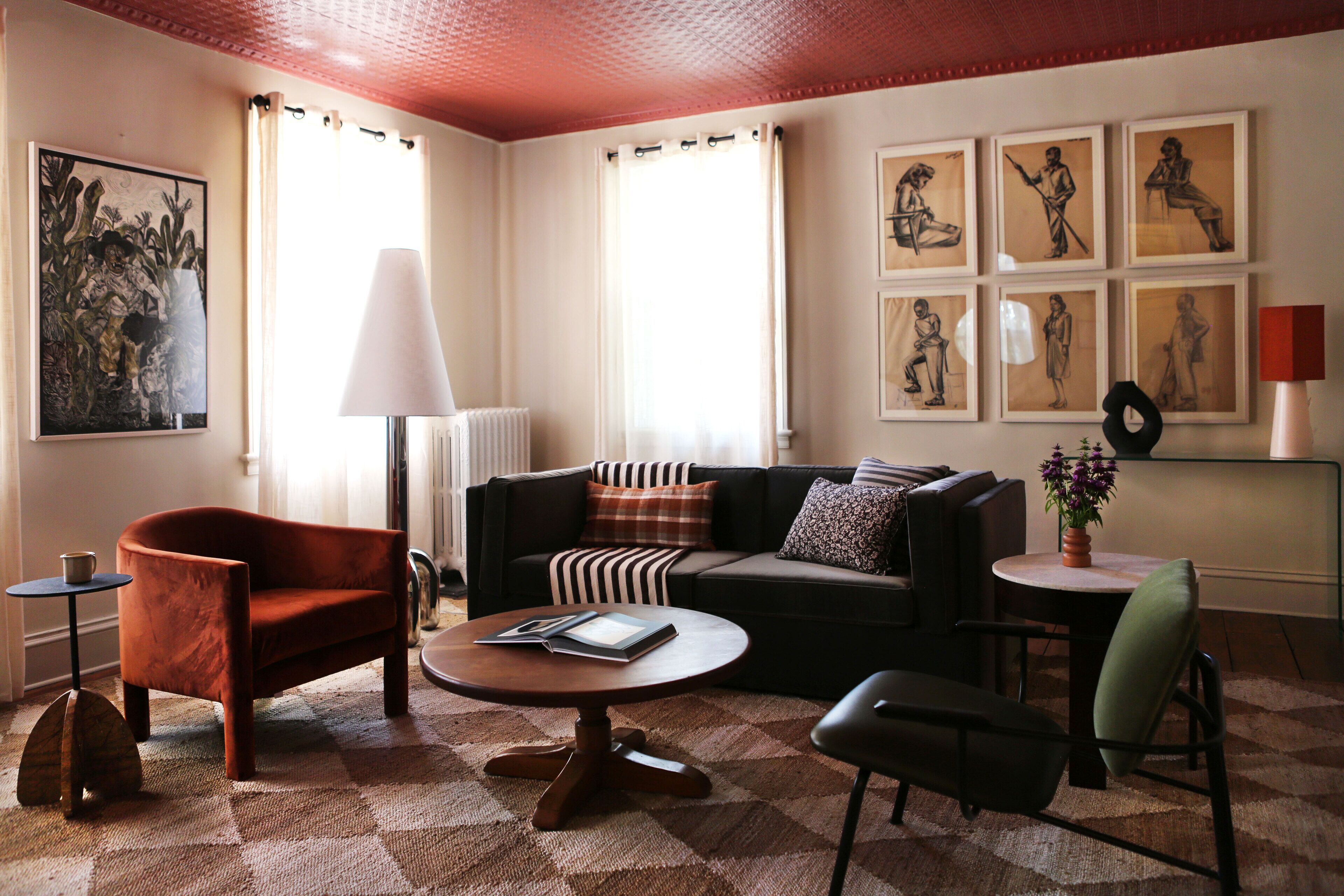A living room with a sofa, armchair, coffee table, and a lamp. There are framed pictures on the wall and a radiator.