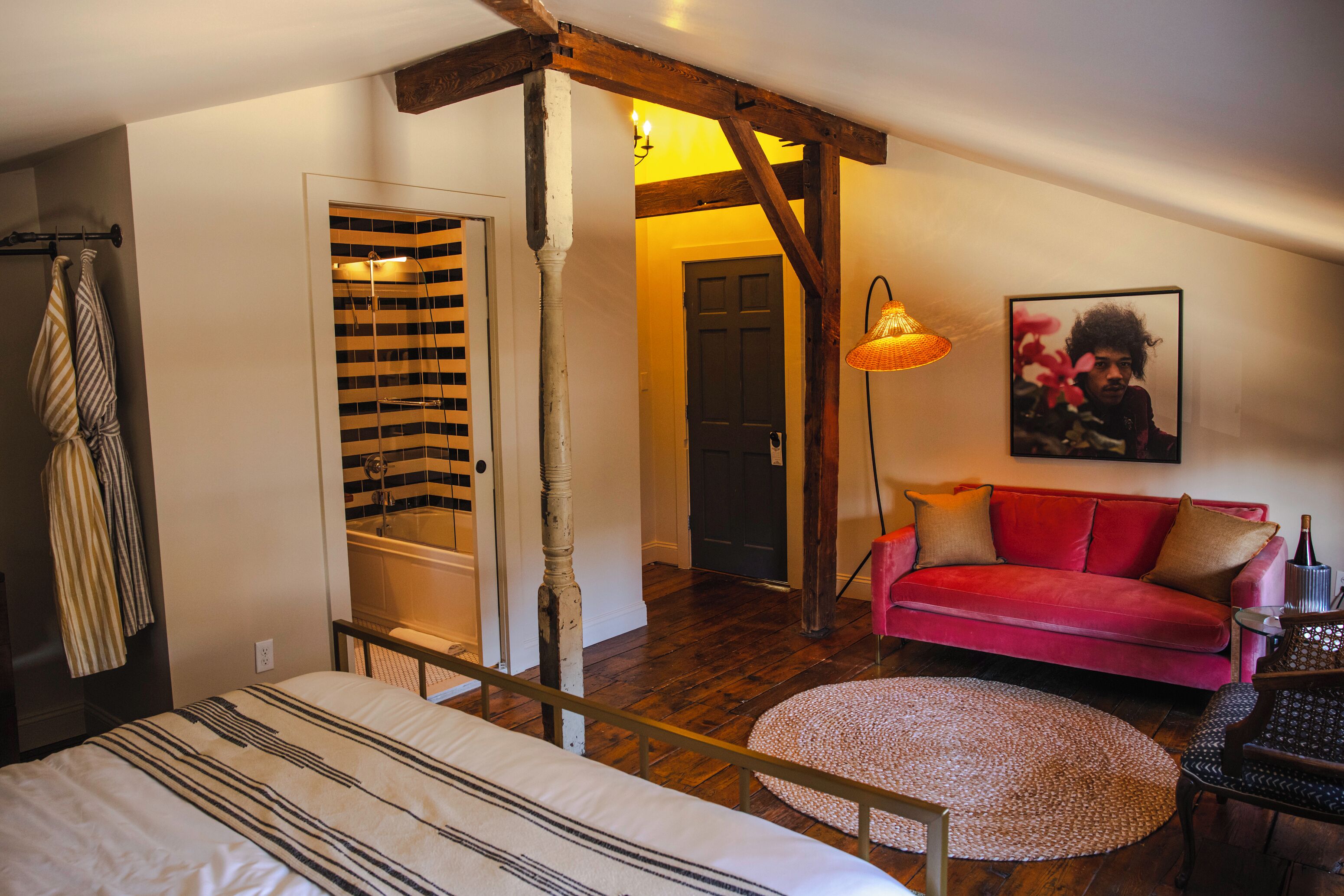 A bedroom with a bed, a red sofa, a round rug, and a wooden ceiling beam.