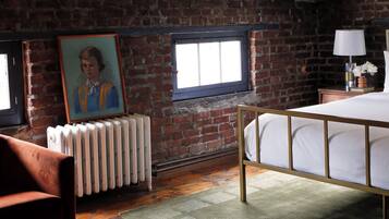 A bedroom with a brick wall, a radiator, a bed, a window, and a painting on the wall.