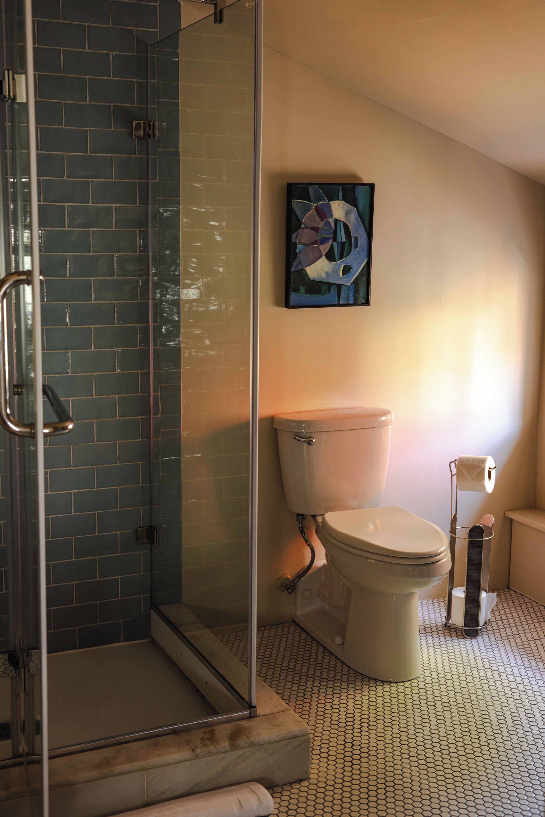 A bathroom with a glass shower enclosure, a toilet, and a wall-mounted painting.