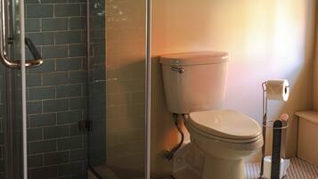 A bathroom with a glass shower enclosure, a toilet, and a wall-mounted painting.