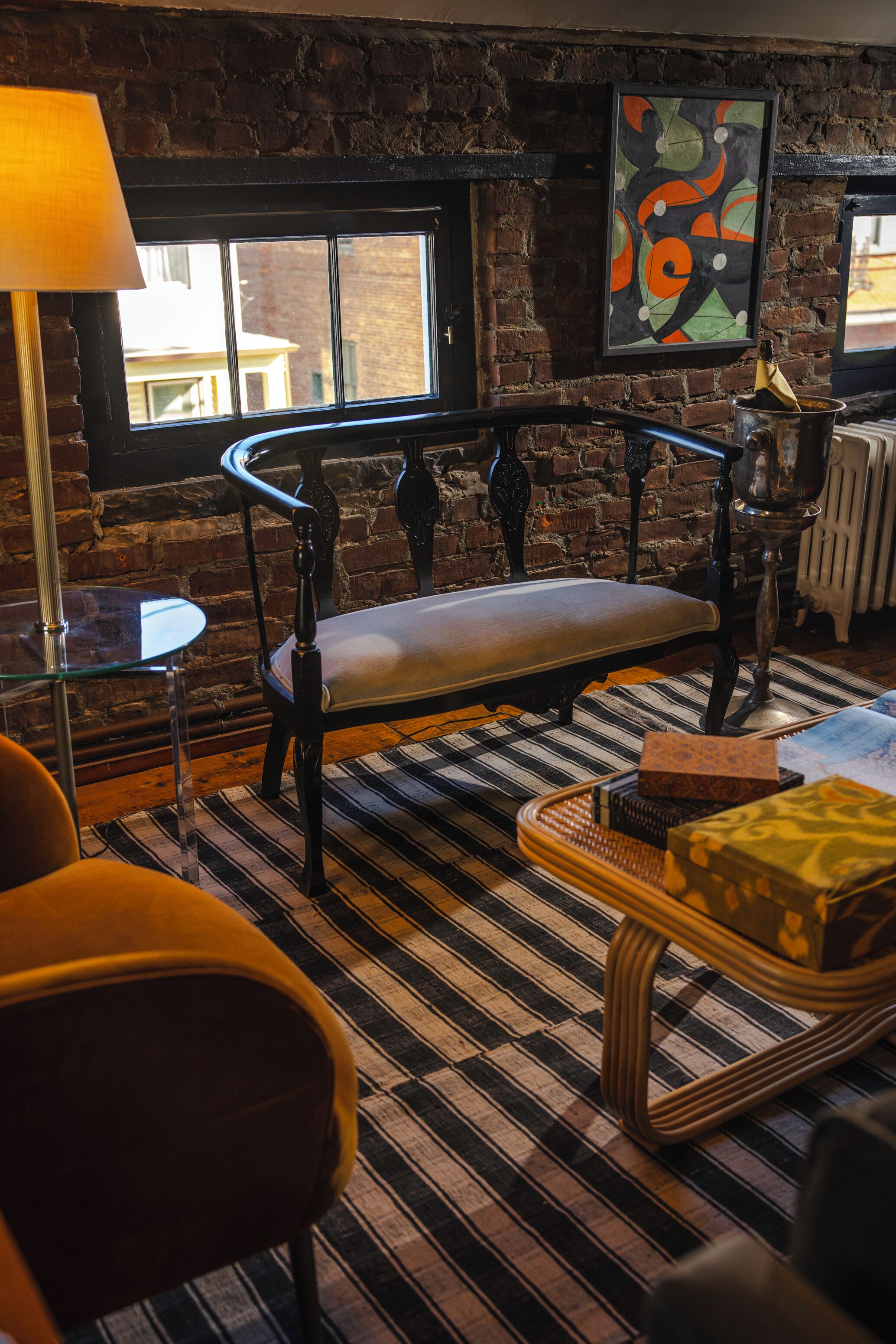 A cozy room with a bench, a small table, a lamp, and a painting on the wall.