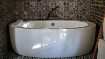 A bathroom with a freestanding bathtub, patterned tiles on the walls, and a wooden floor.