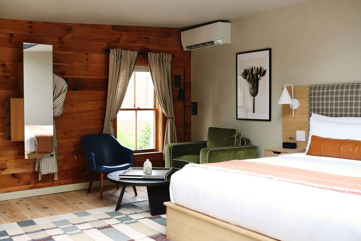 Een hotelkamer met een houten wand, een bed, een bureau, een stoel, een lamp en een schilderij aan de muur.